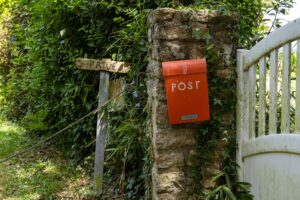 Charming red post box on an ivy-covered stone wall in Brittany, France, near a rustic gate and greenery.