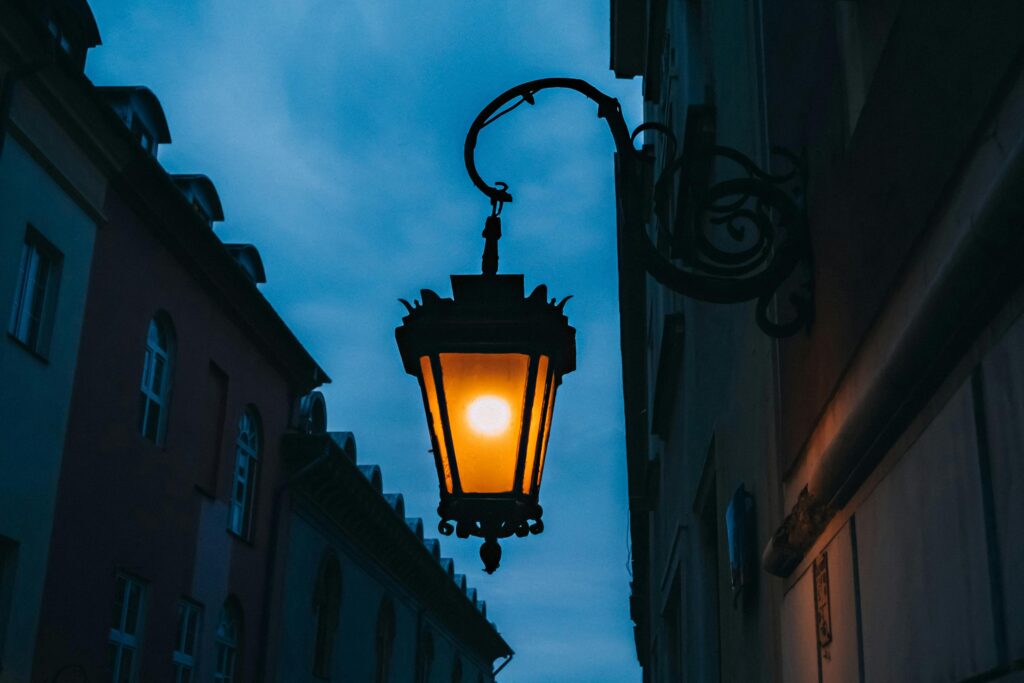 An illuminated streetlamp hangs elegantly between historic buildings as dusk sets in.