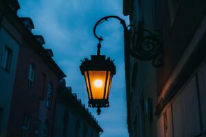 An illuminated streetlamp hangs elegantly between historic buildings as dusk sets in.